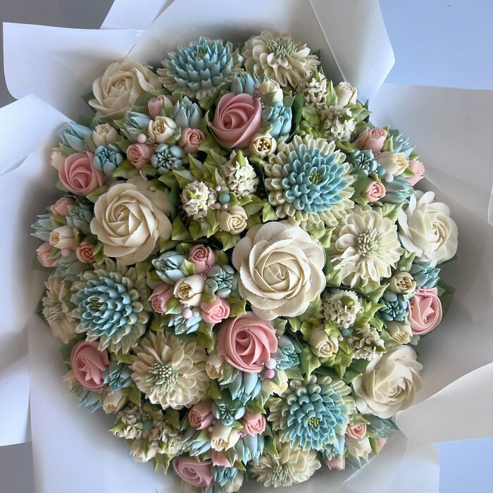 Flower bouquet made of intricately decorated baked goods resembling cupcakes with pastel roses and succulents.