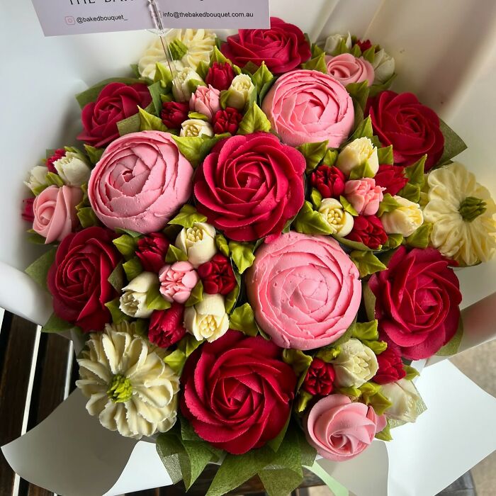 Colorful baked goods resembling flower bouquets with detailed pink, red, and white frosting petals and green leaves in a gift box.
