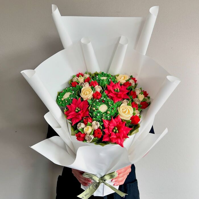 Bouquet of baked goods decorated to look like flower bouquets with red, cream, and green frosting details wrapped in white paper.