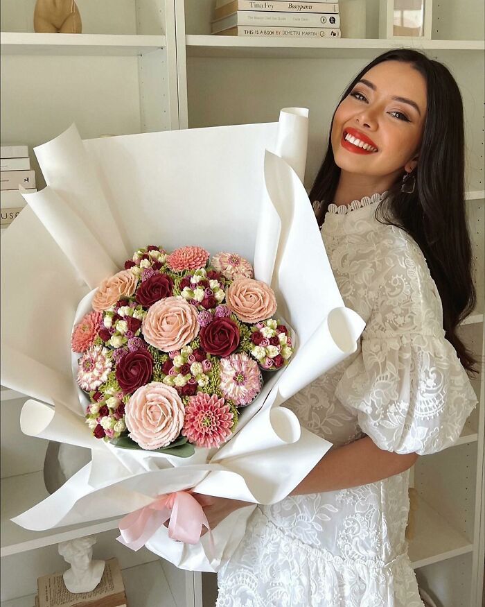 Woman in white lace dress holding a bouquet of baked goods that look like flower bouquets, showcasing edible art.