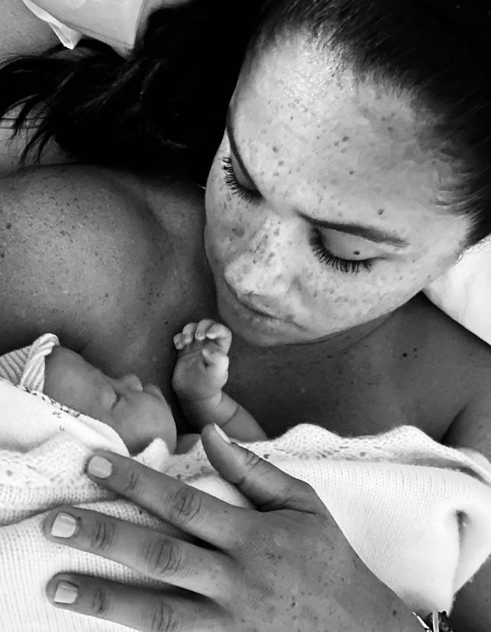 Meghan Markle holding newborn baby close, showcasing intimate mother and child moment in black and white photo.