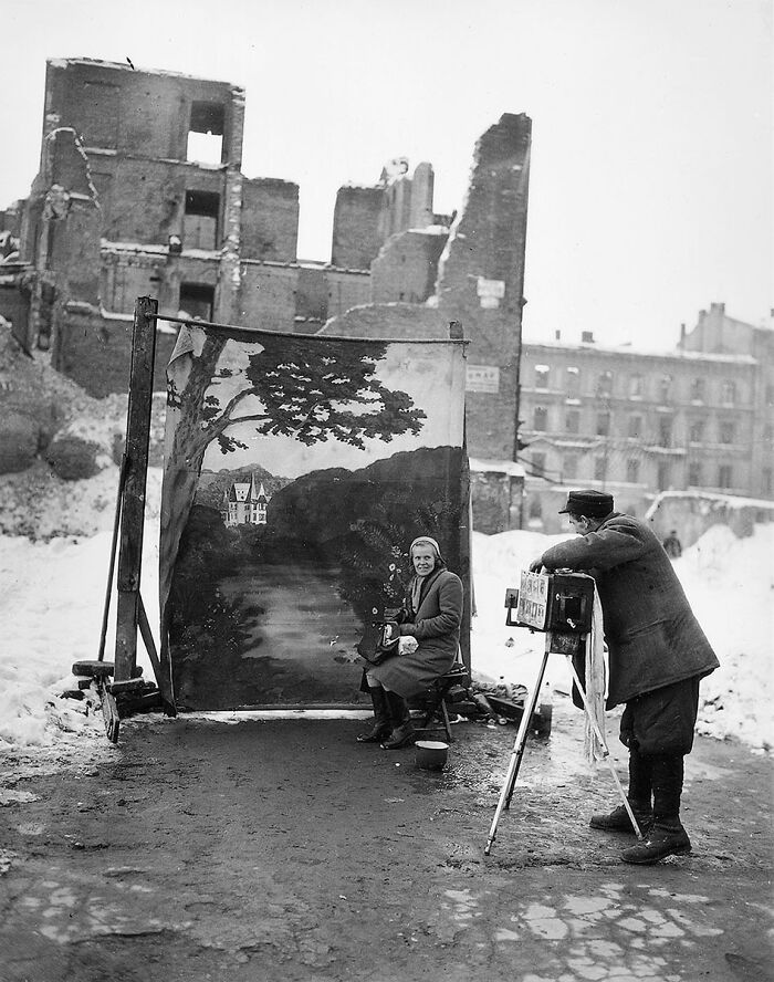 Vintage photo of a street photographer taking pictures in front of a painted backdrop amidst snowy ruins in history.
