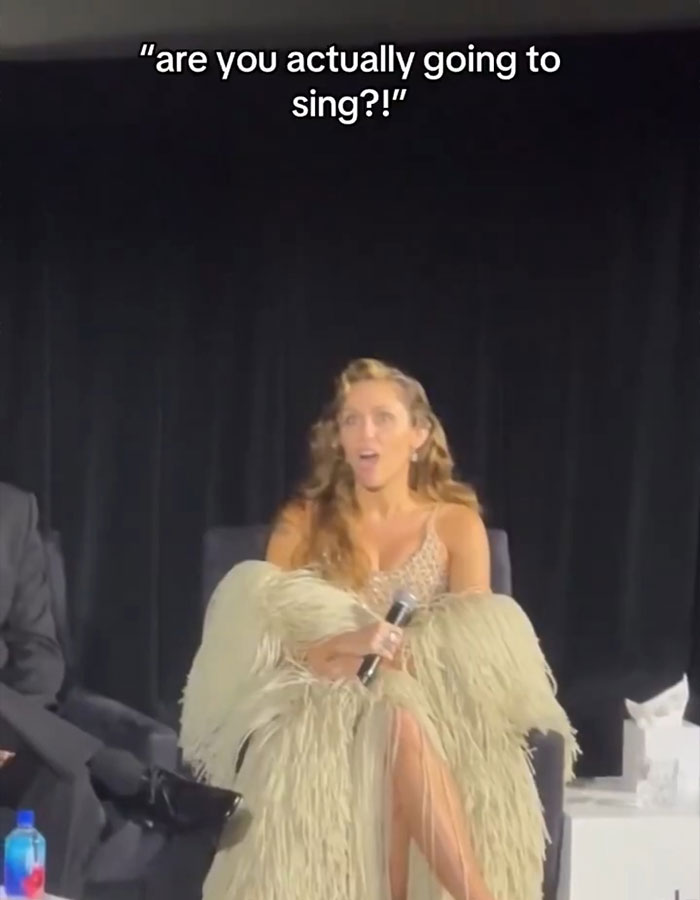 Woman holding microphone looking surprised during Miley Cyrus booed video premiere by fans expecting a concert event