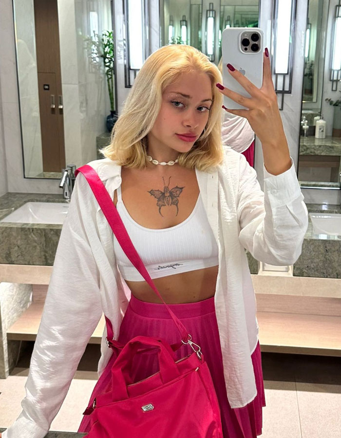 Young model in white top and pink skirt taking a mirror selfie in bathroom after brutal attack in Dubai begins to speak.