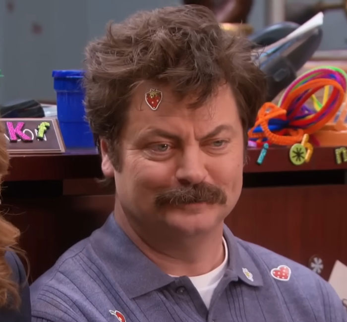 Nick Offerman from Parks and Rec with stickers on his face and shirt reacting in a comedic scene. Nick Offerman from Parks and Rec with stickers on his face and shirt reacting in a comedic scene.