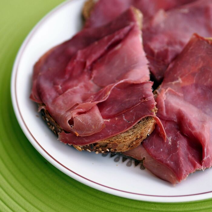 Thin slices of cured meat on multigrain bread representing surprising foods banned in the USA on a white plate.