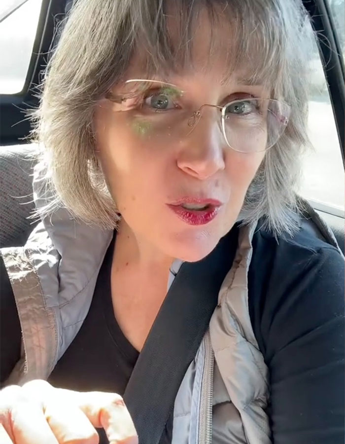 Woman with glasses and gray hair sitting in a car, reacting emotionally to a controversial mom&rsquo;s insulting birthday gift.
