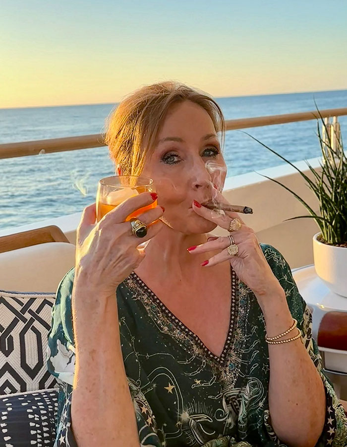 Woman smoking cigar and holding a drink outdoors at sunset, related to J.K. Rowling mocks Pedro Pascal Death Eater claims. Woman smoking cigar and holding a drink outdoors at sunset, related to J.K. Rowling mocks Pedro Pascal Death Eater claims.