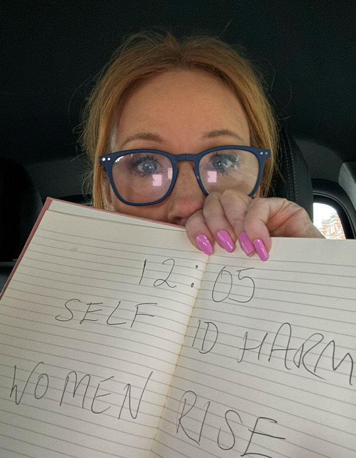 J.K. Rowling wearing glasses and holding a notebook with handwritten text, related to Death Eater and Pedro Pascal. J.K. Rowling wearing glasses and holding a notebook with handwritten text, related to Death Eater and Pedro Pascal.
