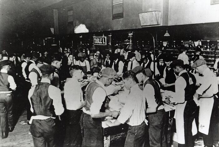 Group of American working class men in vintage factory setting sorting materials at a workstation labeled table 1.