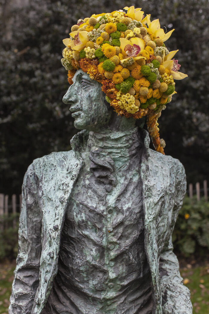 City statue dressed in vibrant yellow and orange flowers, showcasing artistic floral decoration in an urban setting.