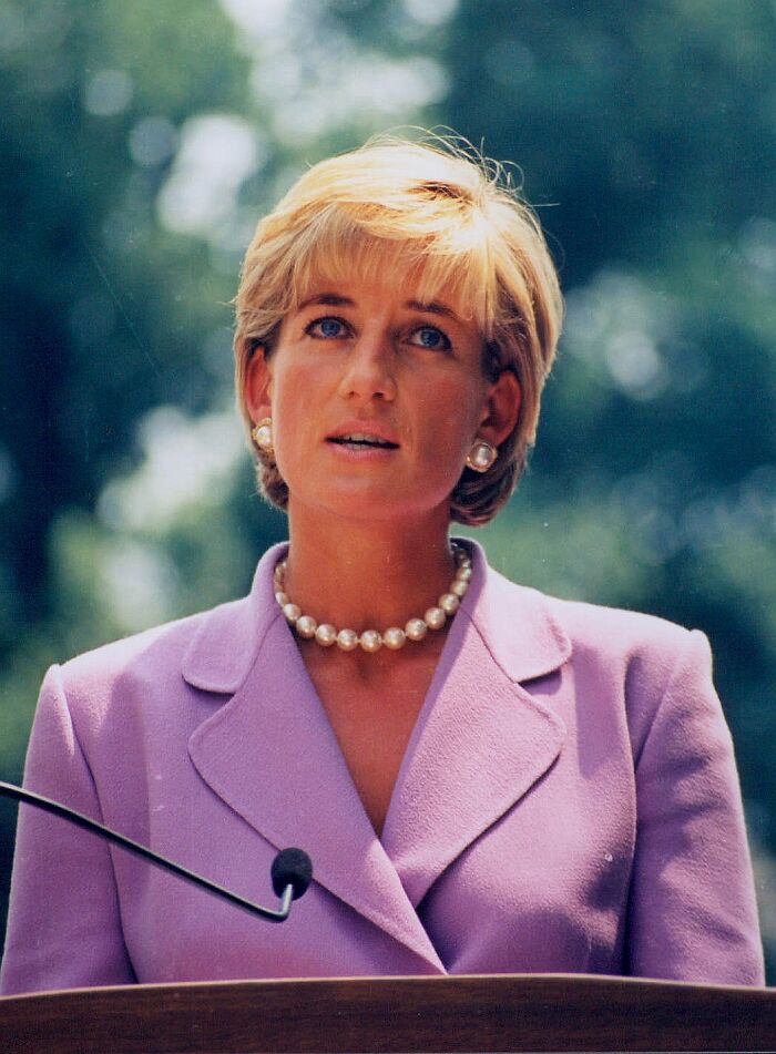 Princess Diana wearing a lavender suit and pearl necklace speaking outdoors with blurred green background facts about Princess Diana.
