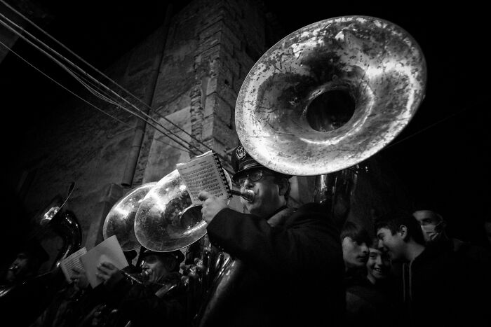 Black and white cinematic photo of musicians playing tubas in a nighttime street scene, capturing everyday life moments.