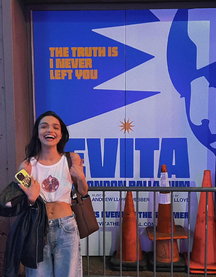 Young woman smiling outside theatrical poster, reflecting Rachel Zegler sparks outrage fans watching on screens after paying 500.