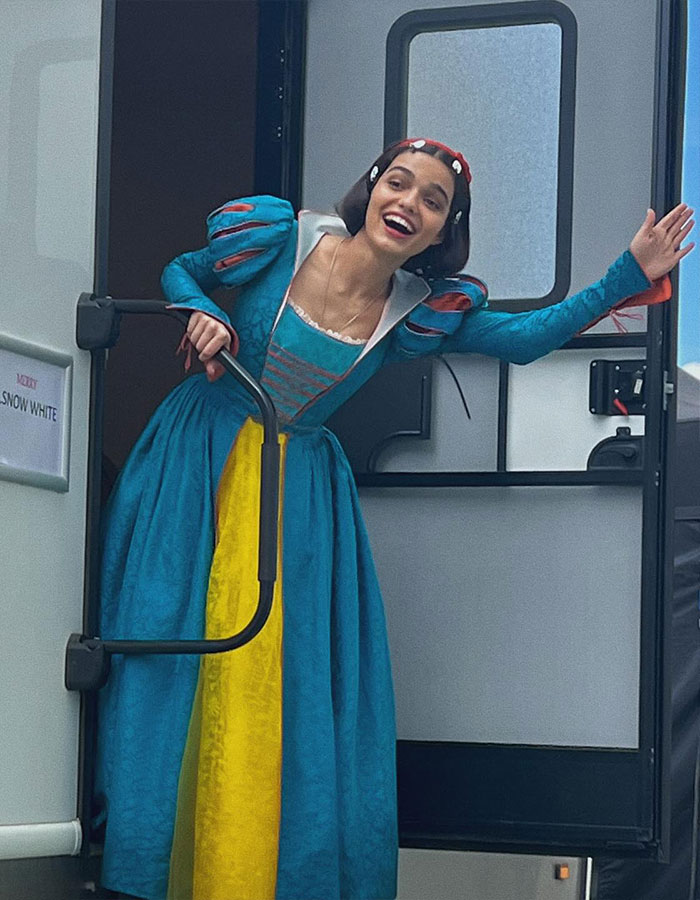 Rachel Zegler wearing Snow White costume, smiling and waving while standing in a trailer doorway during a live show.