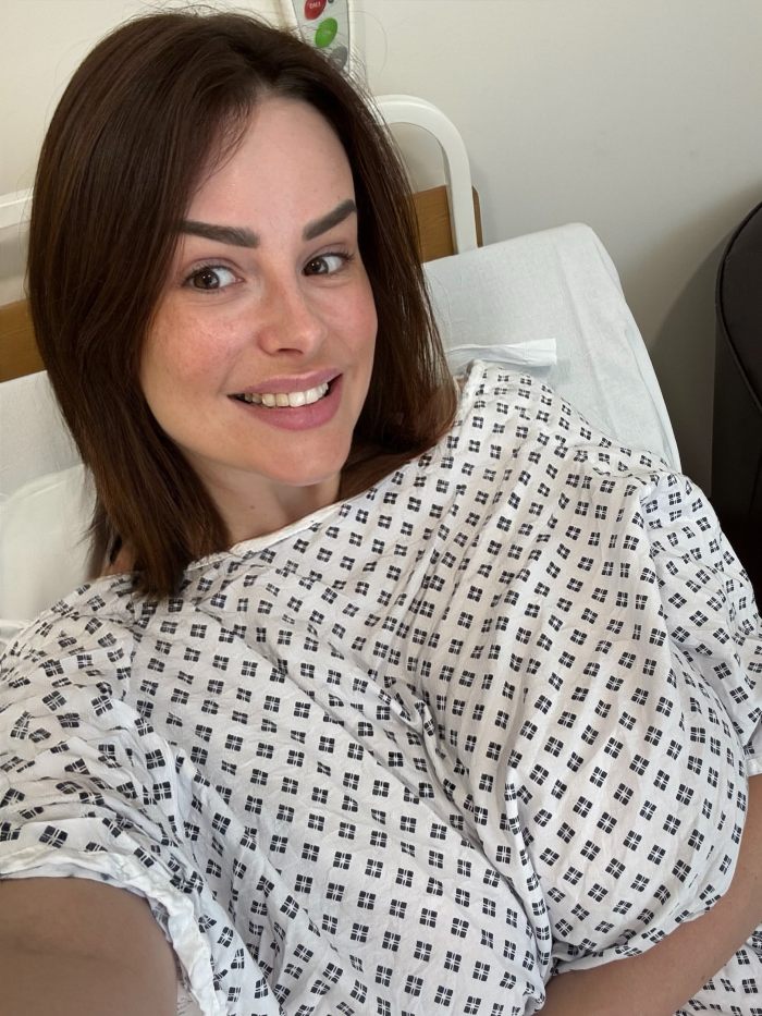 Model with F-Cup chest in hospital gown smiling after breast reduction surgery to ease walking discomfort.