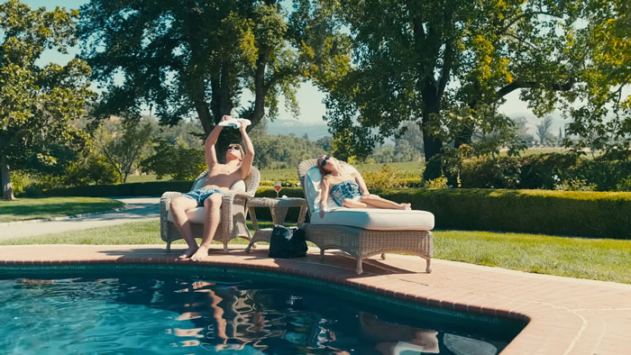 Young adults relaxing by a pool in a luxurious backyard, highlighting nepo grandbaby lifestyle and public criticism.
