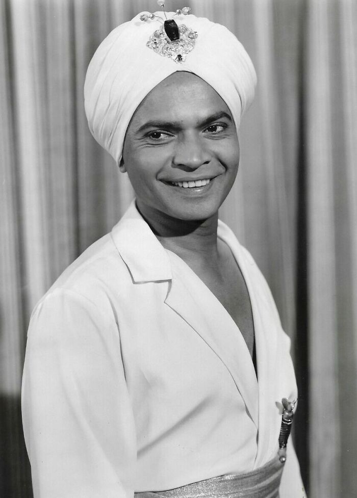 Black and white portrait of a smiling man wearing a jeweled turban and white outfit, symbolizing stars lost too soon.