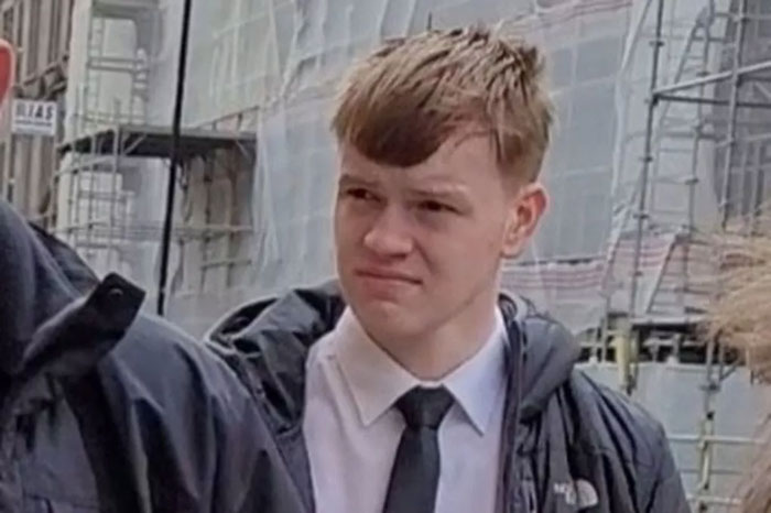 Teen who slammed teacher head-first into concrete wearing white shirt and black tie outdoors near scaffolding.