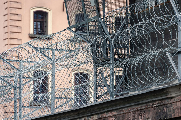 Barbed wire fencing atop prison walls symbolizing the teen who brutally slammed teacher head-first into concrete case.