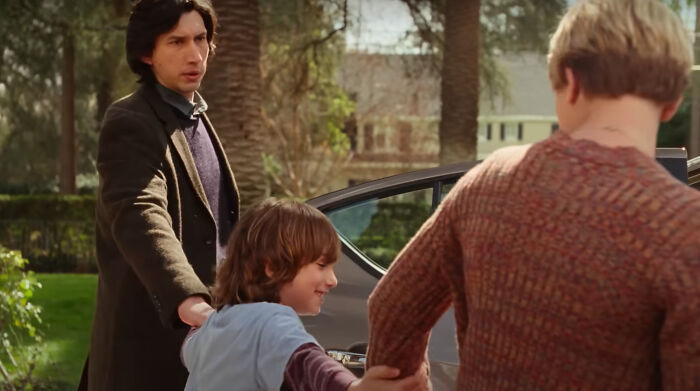 Adam Driver holding a child's hand outdoors near a car, a scene from one of the new millennium's greatest films.