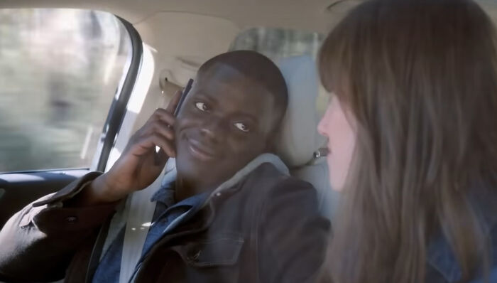 Man speaking on phone while sitting next to woman in car, scene from one of the new millennium's greatest films.