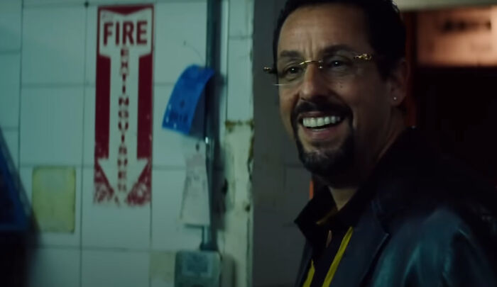 Actor Adam Sandler smiling in a dark room scene from one of the new millennium's greatest films.