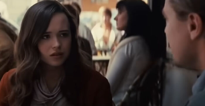 Young woman with long hair looking concerned while talking to a man in a crowded setting, highlighting greatest films.