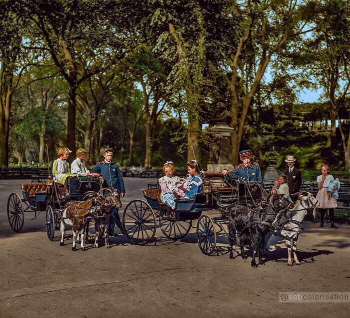 Colorized historical photo of children riding goat-drawn carriages in a park with attendants and onlookers around.