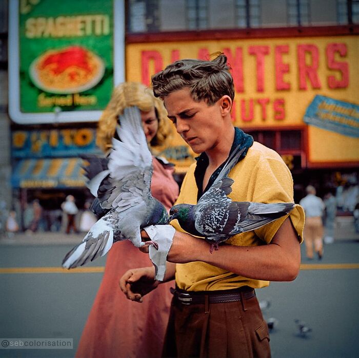 Young man in a yellow shirt feeding pigeons on a busy street, colorized historical photo by a talented viral artist.
