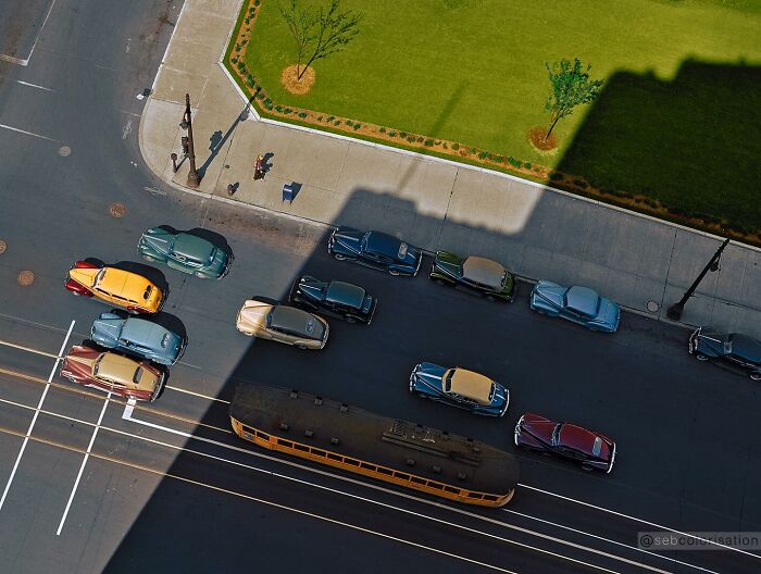 Colorized historical photo showing vintage cars and a tram on a city street from a top-down perspective.