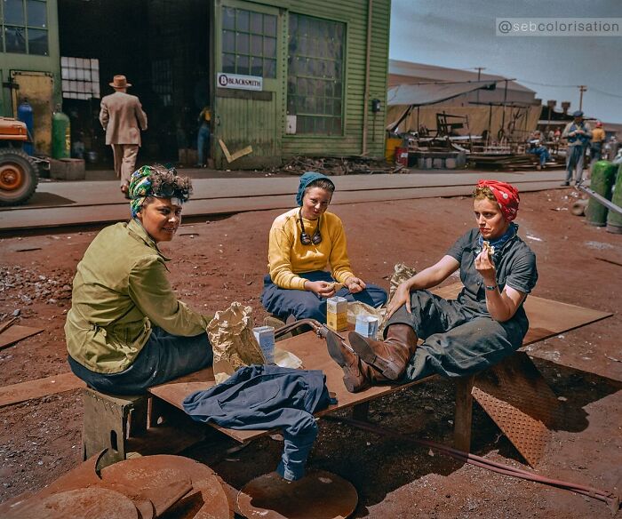 Three women on a break at a workshop, colorized historical photo showing workers in vintage clothing and industrial setting.