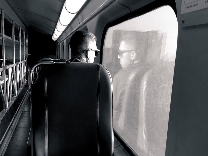Man wearing sunglasses seated inside a train, reflecting in the window, capturing Chicago street life and city soul.