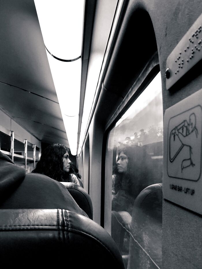 Woman sitting on a train, her face reflected in the window, captured in a candid Chicago street photo revealing the city’s soul.