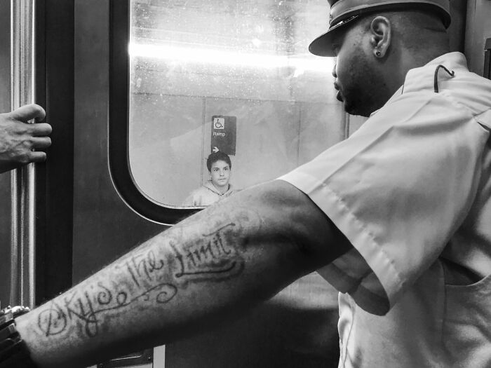 Black and white street photo capturing a Chicago transit worker with an arm tattoo and a passenger outside the train door.