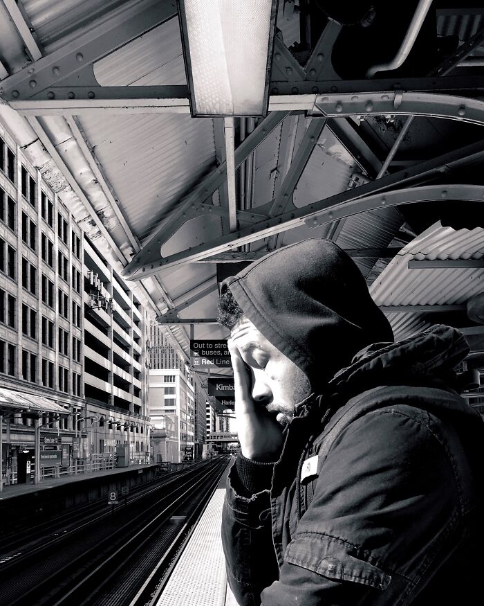Man in a hooded jacket at a Chicago train station platform, capturing intimate street moment in urban setting.