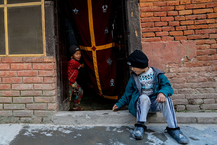 Two children playing outside a brick doorway, capturing candid street photos of everyday life moments.