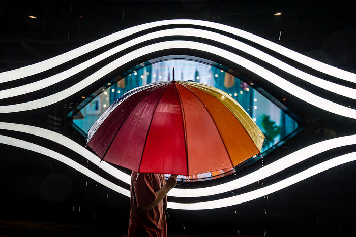 Person holding a colorful umbrella in the rain, captured in a candid street photo that shows everyday life beauty.