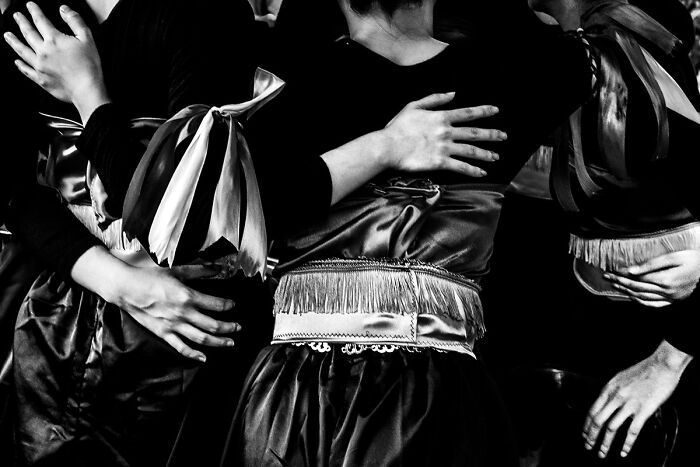 Candid street photo capturing the quiet beauty of everyday life with close-up on intertwined hands and traditional costumes.