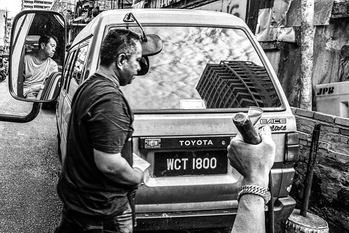 Candid street photo showing a man walking past a Toyota car, capturing the quiet beauty of everyday life in black and white.