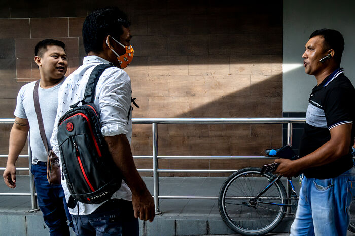 Three men casually talking on a city street by a bicycle, capturing candid street photos of everyday life.