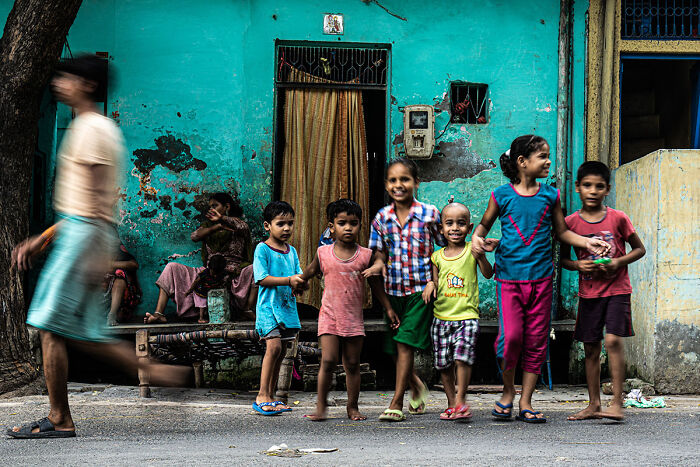 Group of children smiling and playing outside a weathered turquoise building in a candid street photo capturing everyday life.