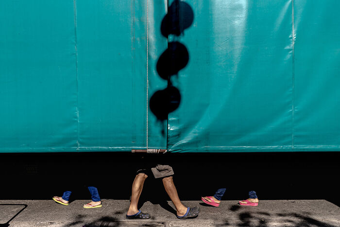 Legs of people walking by a teal wall, captured in candid street photos highlighting quiet beauty of everyday life.