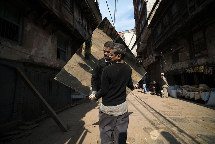 Man carrying a large mirror through a narrow street in a candid street photo capturing everyday life moments.