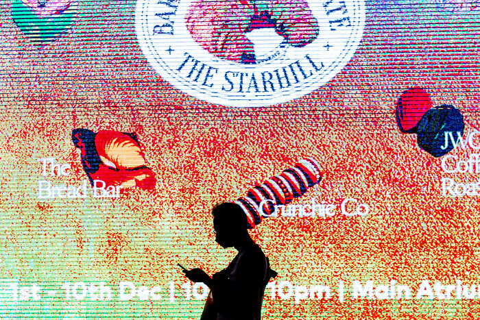 Silhouette of a person using a phone against a colorful digital street photo capturing the quiet beauty of everyday life.