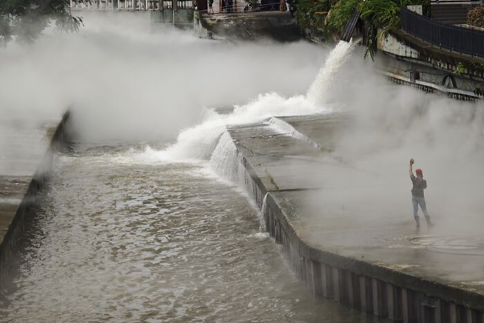 Person walking near misty riverbank with rushing water, capturing quiet beauty in candid street photos.