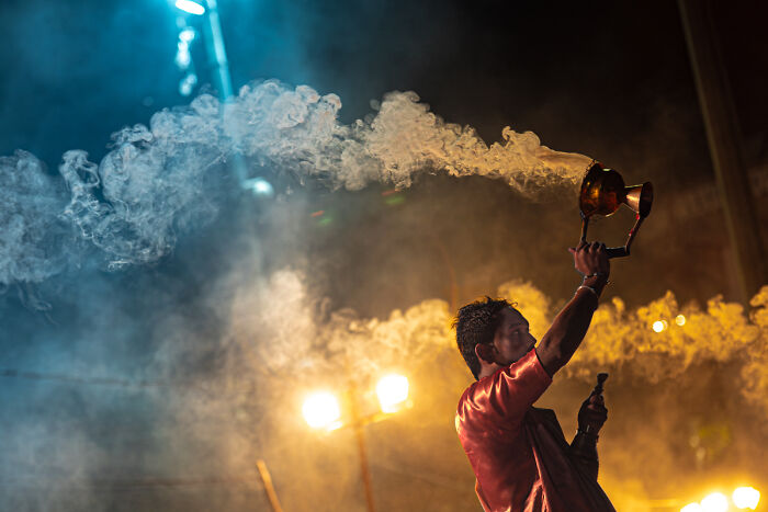 A candid street photo capturing the quiet beauty of everyday life with smoke and warm lighting at night.
