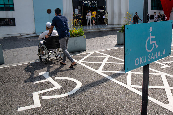 Man pushing elderly person in wheelchair across street in a candid street photo capturing quiet beauty of everyday life