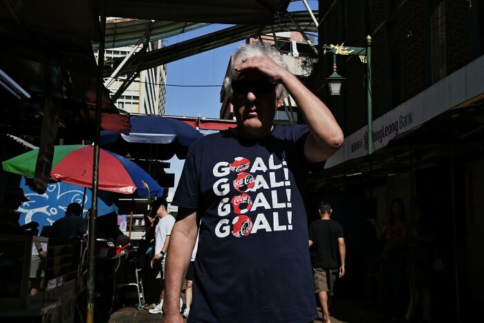 Man shielding his eyes from the sun in a candid street photo capturing the quiet beauty of everyday life.