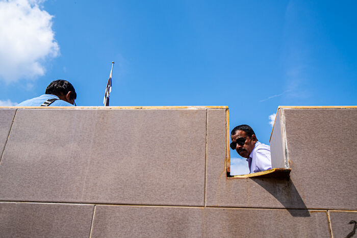 Two men partially visible behind a wall under a bright blue sky in candid street photos capturing everyday life.
